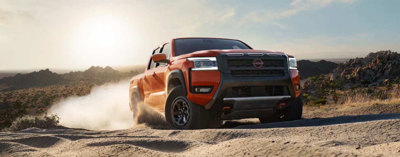 Orange 2026 Nissan Frontier driving on a dirt road