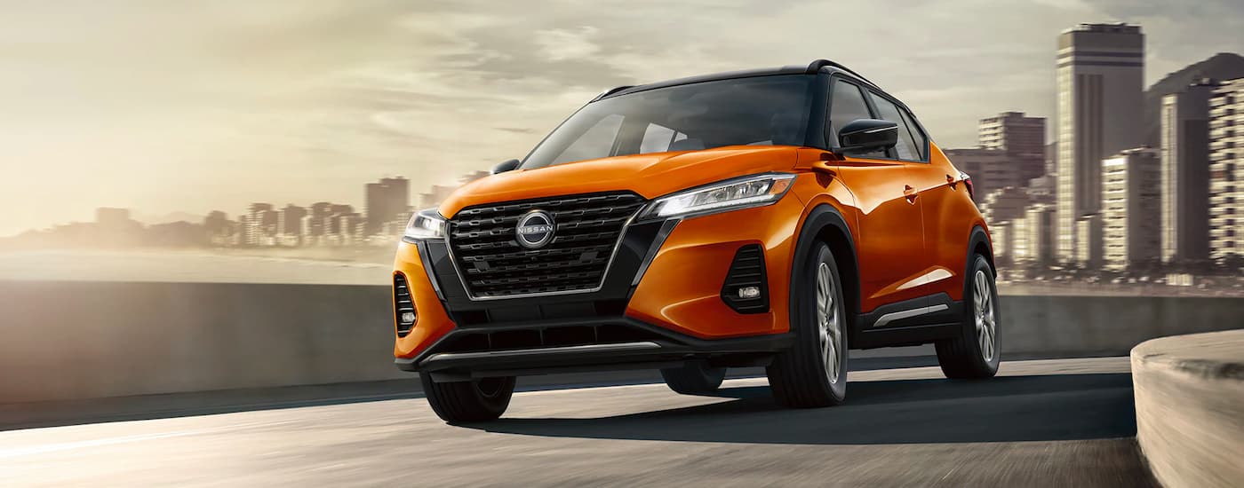 An orange 2023 Nissan Kicks SR driving away from a city.